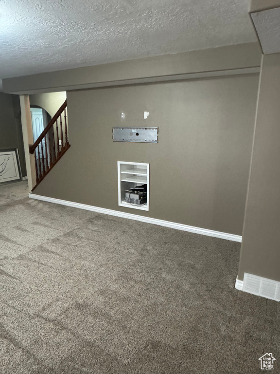 Basement featuring carpet, a textured ceiling, baseboards, and stairs