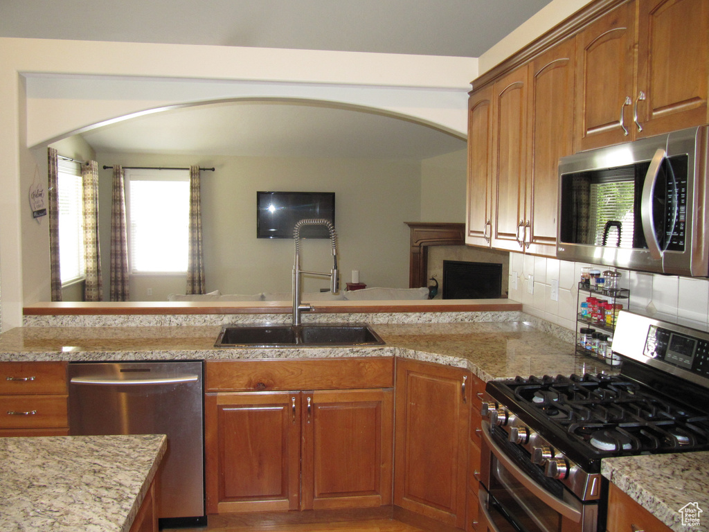 Kitchen featuring stainless steel appliances, a sink, arched walkways, and brown cabinetry