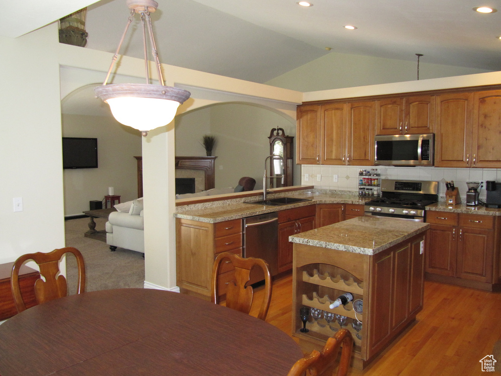 Kitchen featuring appliances with stainless steel finishes, light stone counters, vaulted ceiling, brown cabinets, and backsplash