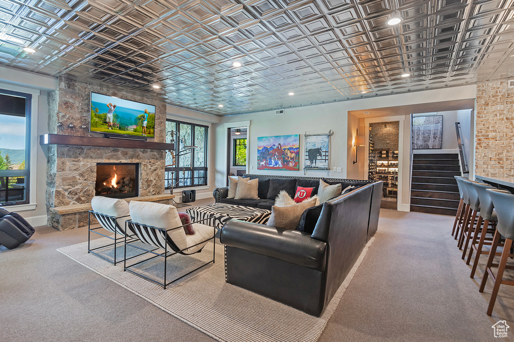 Carpeted living room with an ornate ceiling, a stone fireplace, stairs, baseboards, and recessed lighting