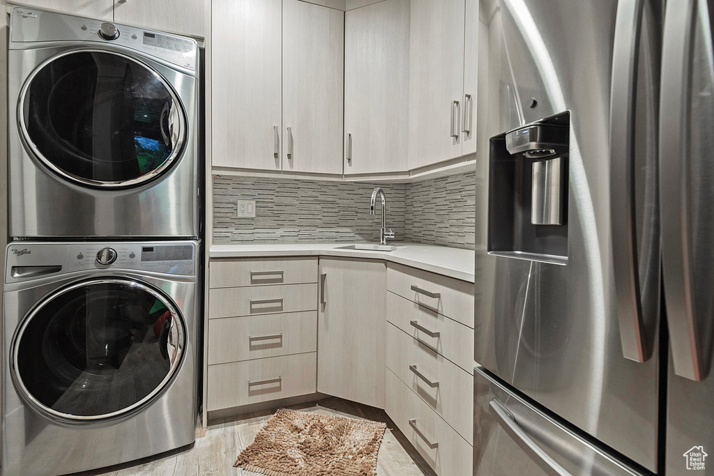 Washroom with stacked washing machine and dryer and light wood-style flooring