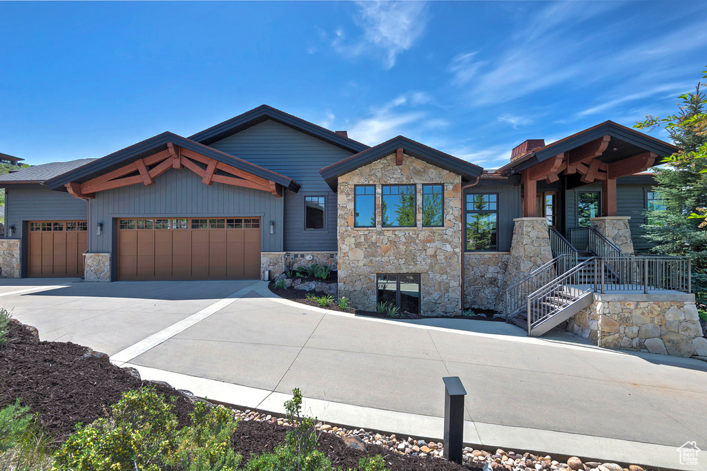 View of front facade with stone siding, an attached garage, driveway, and a chimney