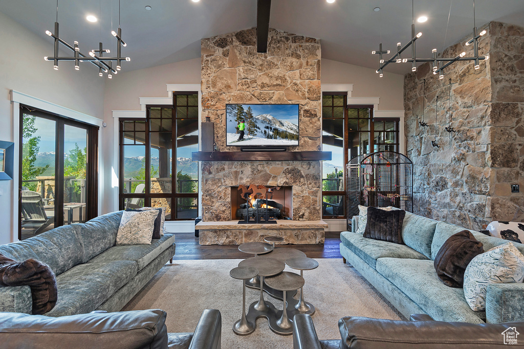 Living area with a stone fireplace, a chandelier, wood finished floors, beam ceiling, and high vaulted ceiling