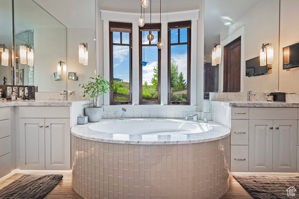 Full bath featuring two vanities, a bath, and wood finished floors