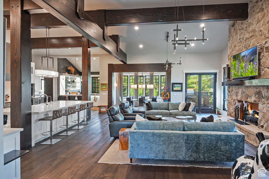 Living room featuring beam ceiling, dark wood finished floors, a stone fireplace, a towering ceiling, and a chandelier