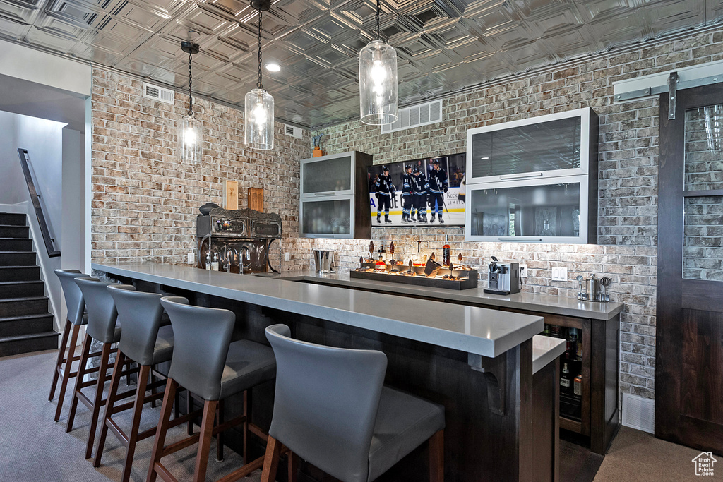 Indoor wet bar with an ornate ceiling, brick wall, stairs, and pendant lighting