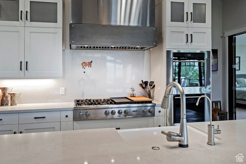 Kitchen featuring range hood, appliances with stainless steel finishes, white cabinetry, glass insert cabinets, and a sink