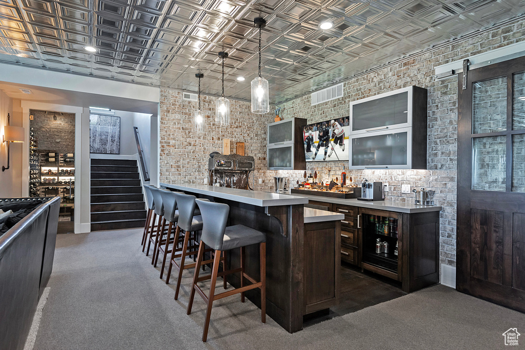 Indoor wet bar with an ornate ceiling, stairway, hanging light fixtures, brick wall, and dark colored carpet