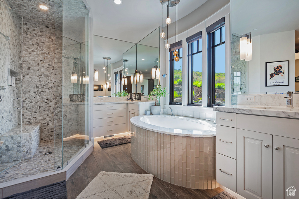 Bathroom featuring a shower stall, a garden tub, wood finished floors, two vanities, and recessed lighting
