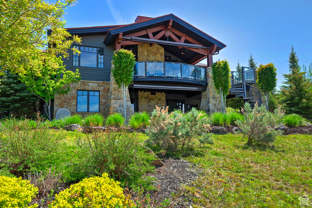 Rear view of house featuring stone siding, stairway, and a balcony