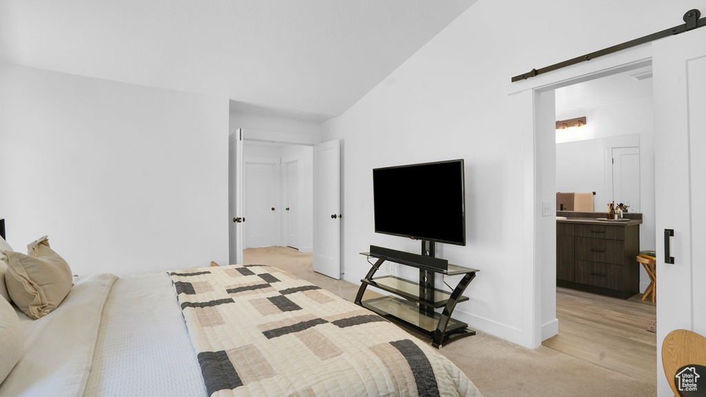 Bedroom with a barn door, light colored carpet, ensuite bath, and baseboards