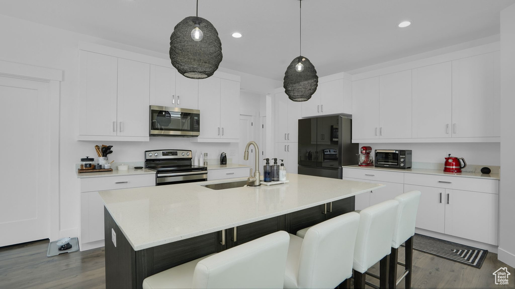 Kitchen featuring appliances with stainless steel finishes, dark wood-type flooring, a breakfast bar, decorative light fixtures, and recessed lighting