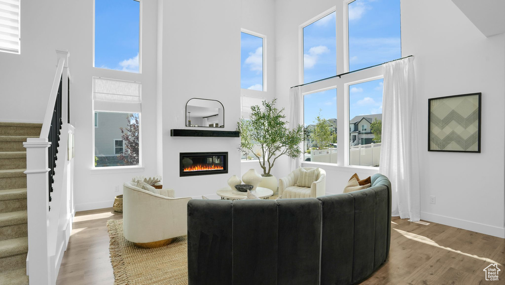 Living room featuring a towering ceiling, a glass covered fireplace, stairs, wood finished floors, and healthy amount of natural light