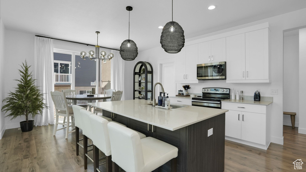 Kitchen featuring stainless steel appliances, a sink, a kitchen island with sink, dark wood-type flooring, and baseboards