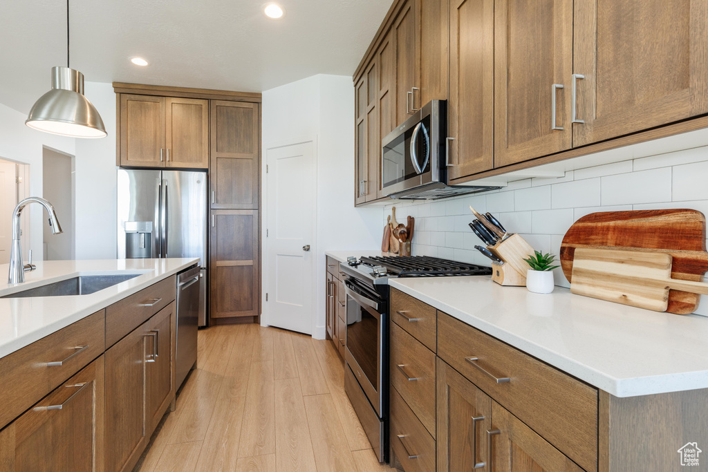 Kitchen with appliances with stainless steel finishes, light wood-type flooring, a sink, decorative backsplash, and brown cabinetry