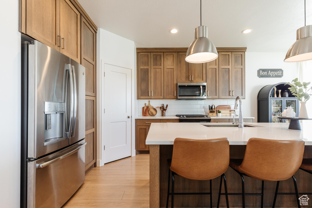 Kitchen featuring stainless steel appliances, a sink, light countertops, decorative backsplash, and light wood finished floors