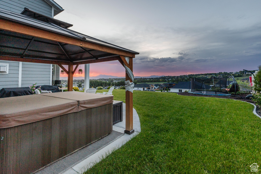 Yard at dusk featuring a hot tub, a gazebo, a trampoline, and a yard