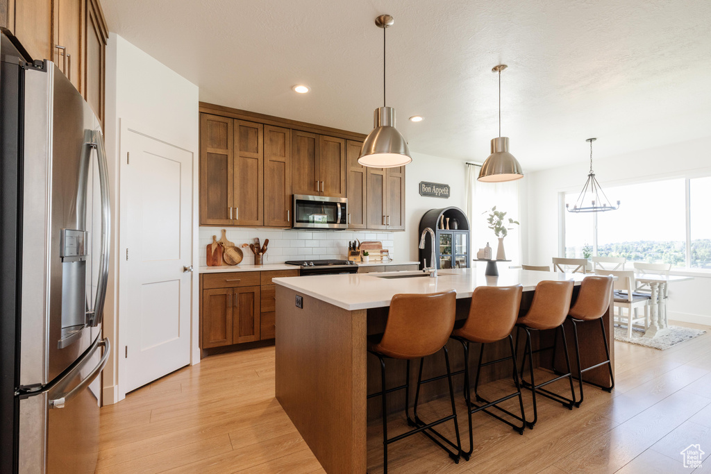 Kitchen with stainless steel appliances, brown cabinetry, a sink, light wood-style flooring, and decorative backsplash