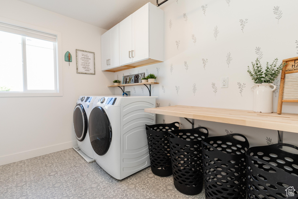 Laundry room with washing machine and clothes dryer, light floors, cabinet space, and baseboards