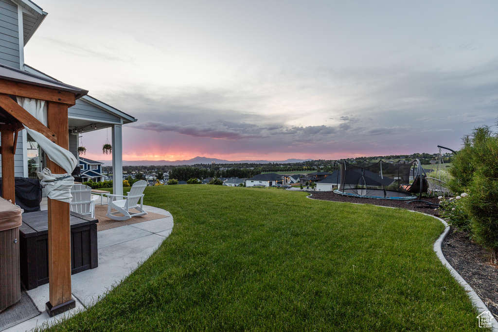 Yard at dusk featuring a trampoline, a patio, and a lawn