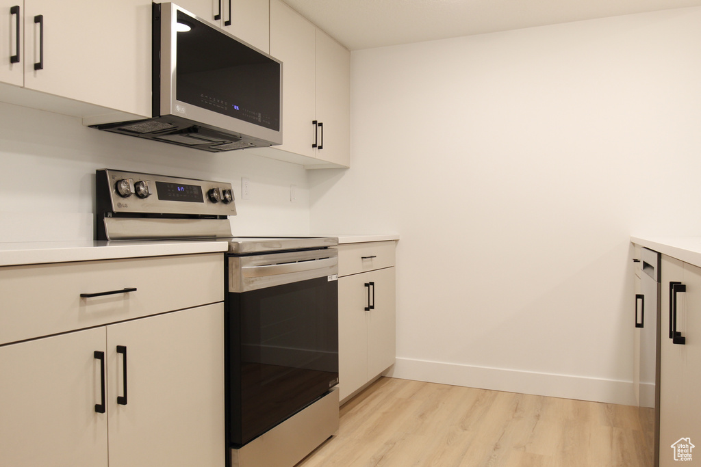 Kitchen featuring electric stove, light wood finished floors, white cabinets, and light countertops