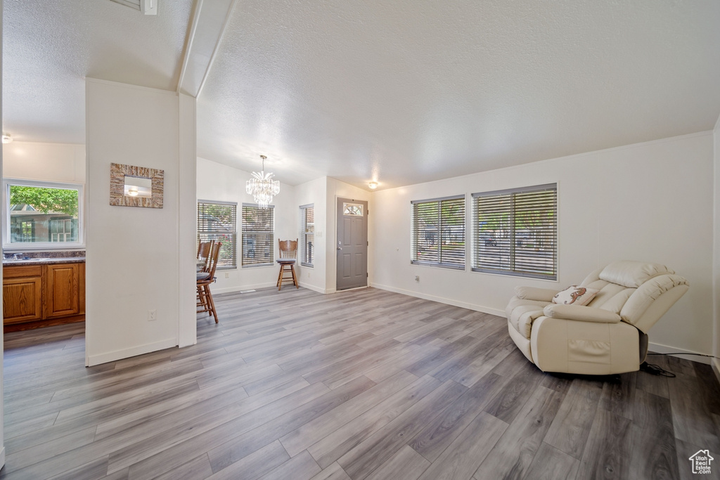Unfurnished room featuring a chandelier, light wood-style floors, a textured ceiling, baseboards, and lofted ceiling