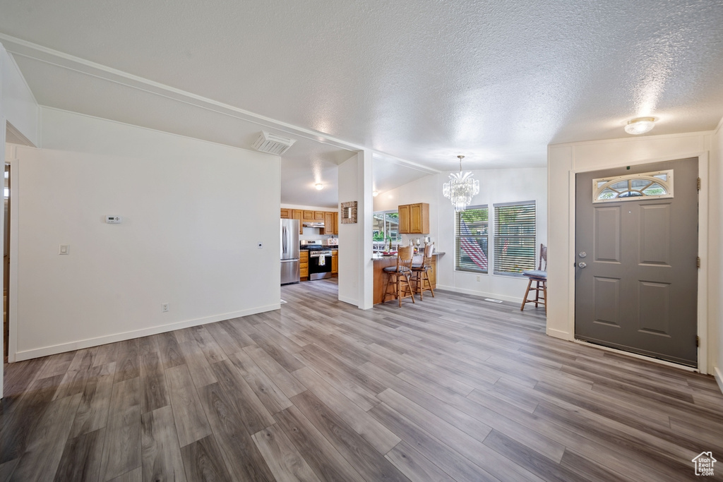 Unfurnished living room featuring wood finished floors, a chandelier, a textured ceiling, baseboards, and vaulted ceiling