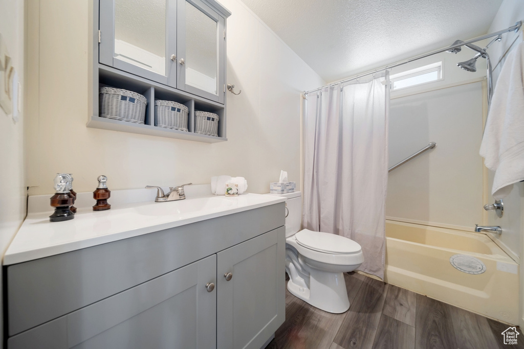 Full bath with shower / bath combo with shower curtain, vanity, toilet, wood finished floors, and a textured ceiling