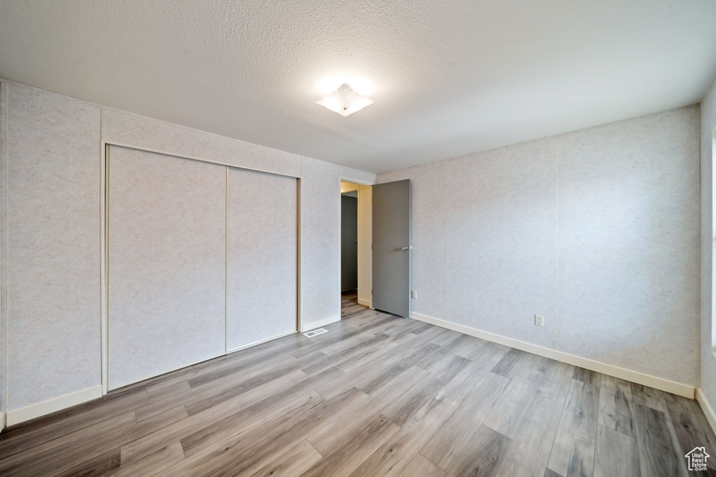 Unfurnished bedroom featuring light wood-style flooring, a closet, baseboards, and a textured ceiling