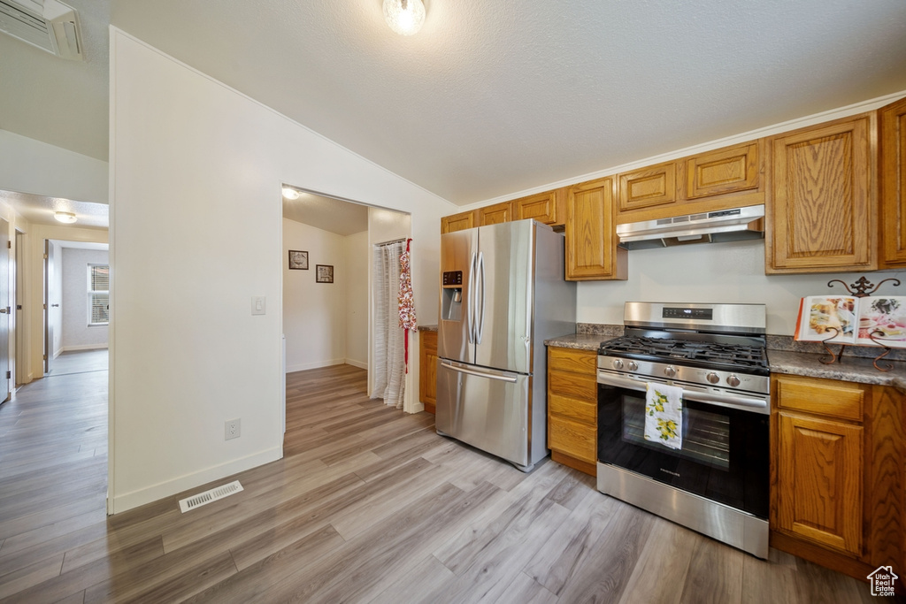 Kitchen featuring stainless steel appliances, under cabinet range hood, lofted ceiling, light wood-style flooring, and brown cabinetry