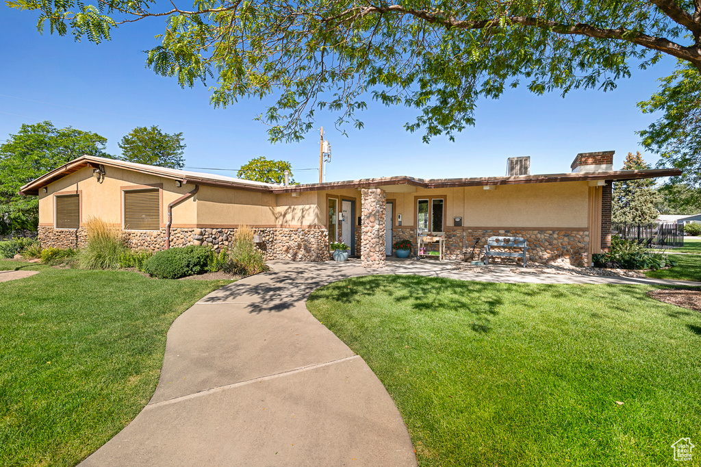 View of front of home featuring stone siding, stucco siding, a front lawn, and a patio