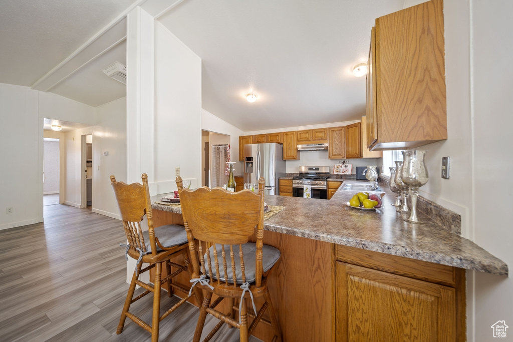 Kitchen with stainless steel appliances, under cabinet range hood, a peninsula, light wood-type flooring, and brown cabinets