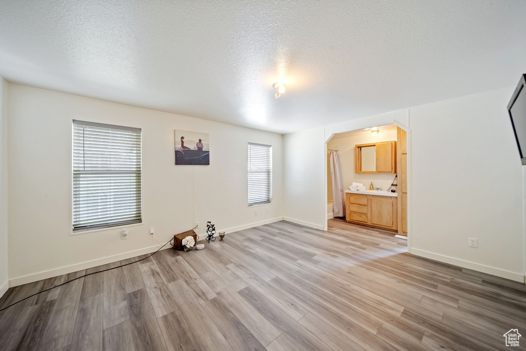 Unfurnished bedroom featuring arched walkways, light wood finished floors, baseboards, a textured ceiling, and connected bathroom