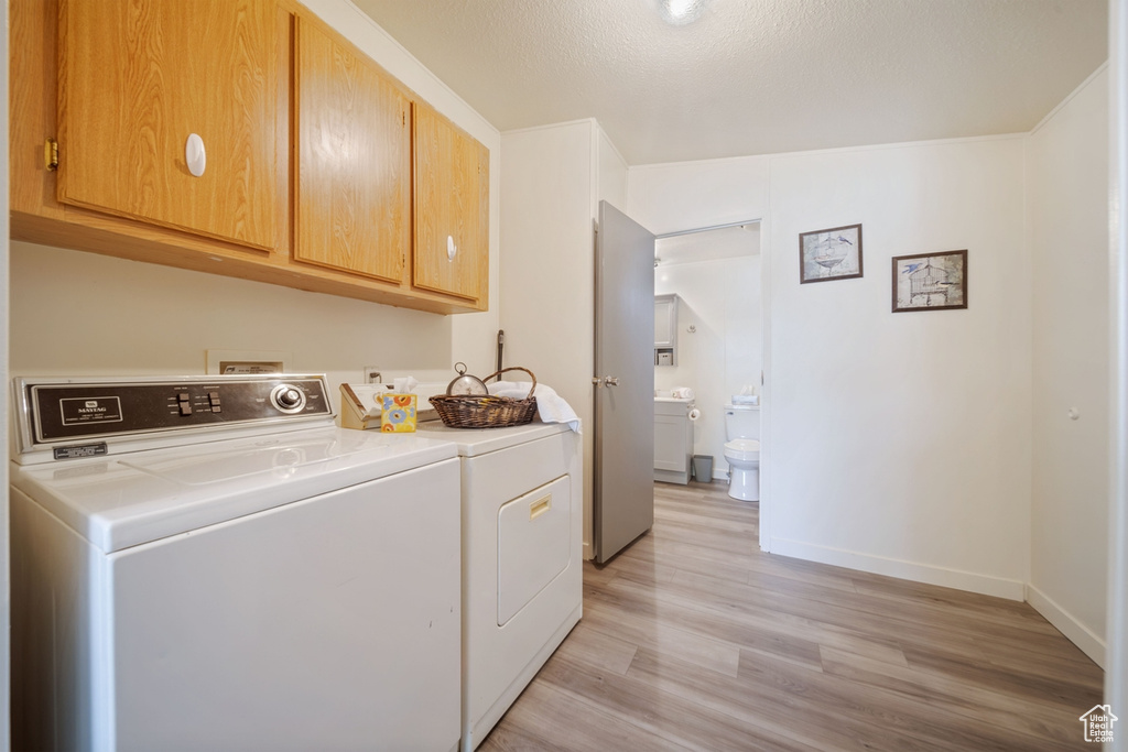 Laundry room featuring cabinet space, light wood-style floors, washer and dryer, and baseboards