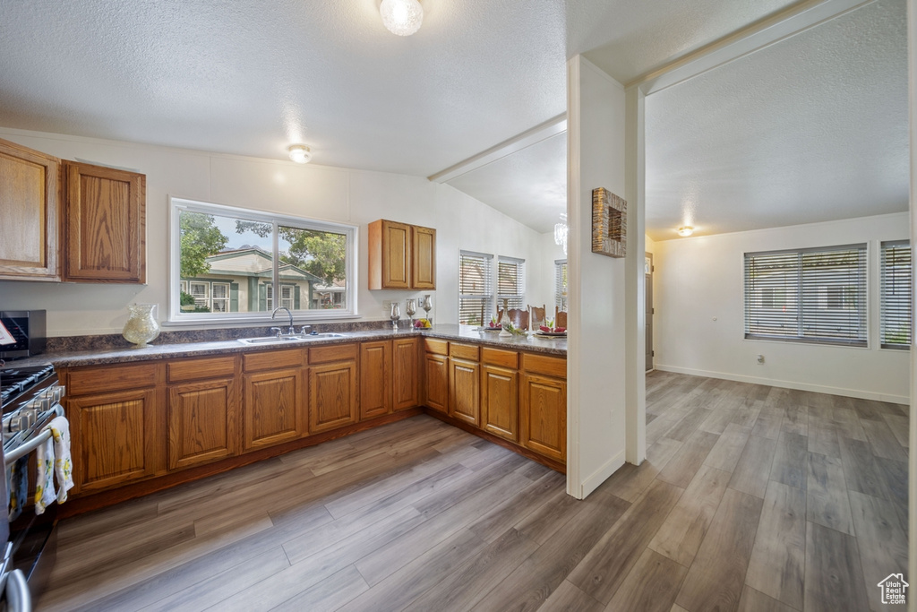 Kitchen with gas range, vaulted ceiling, brown cabinets, light wood-style floors, and a sink