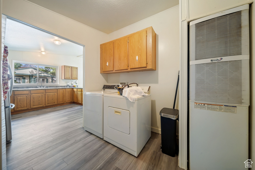 Laundry room featuring a heating unit, cabinet space, washing machine and dryer, and light wood-style floors
