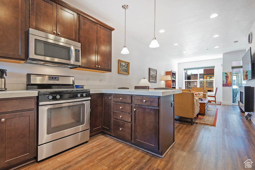 Kitchen featuring stainless steel appliances, wood finished floors, light countertops, a peninsula, and dark brown cabinetry