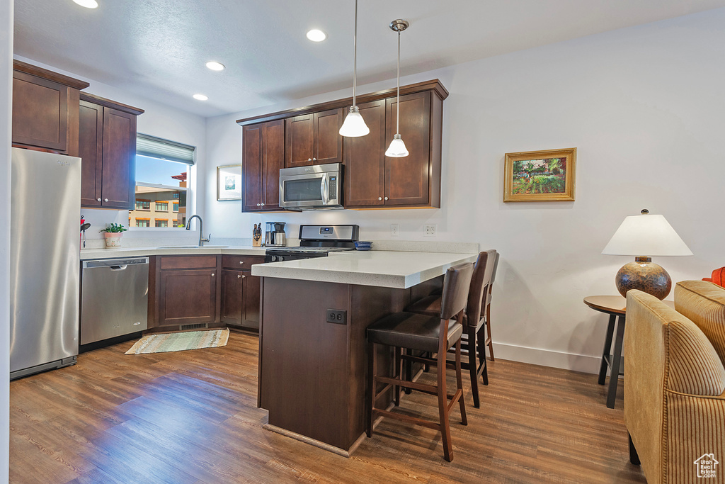 Kitchen with stainless steel appliances, a peninsula, a kitchen breakfast bar, dark wood-style floors, and recessed lighting