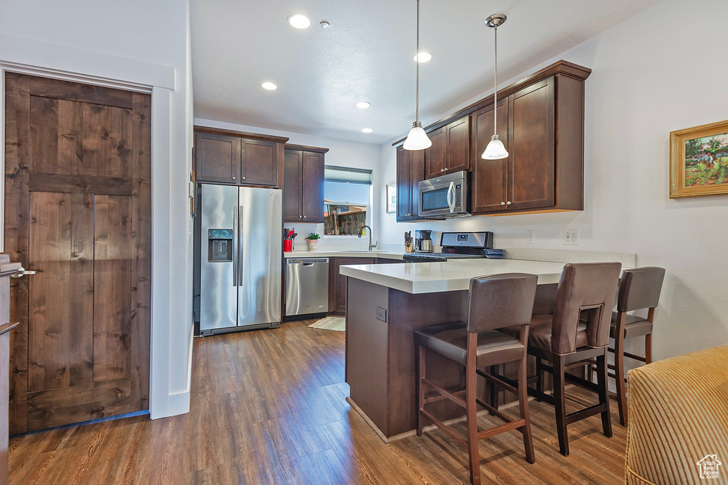 Kitchen with stainless steel appliances, dark brown cabinetry, dark wood-style flooring, a peninsula, and a breakfast bar area