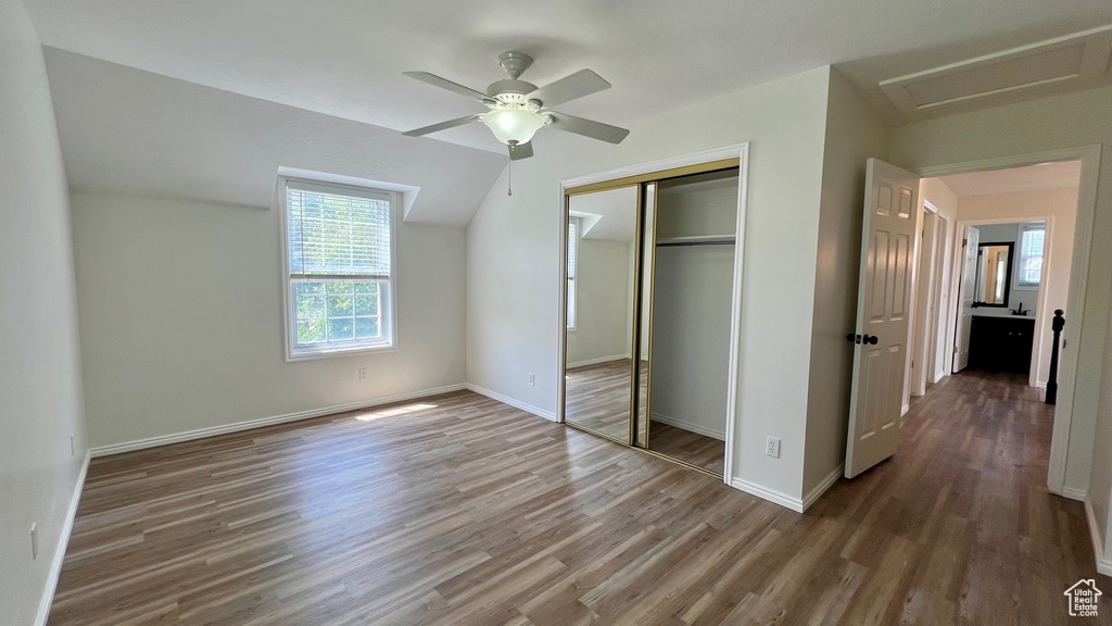 Unfurnished bedroom with wood finished floors, a closet, attic access, and baseboards