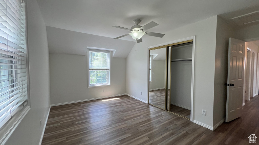 Unfurnished bedroom featuring dark wood-style flooring, a closet, baseboards, ceiling fan, and lofted ceiling