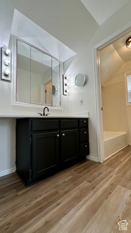 Full bath with vaulted ceiling, vanity, wood finished floors, and baseboards