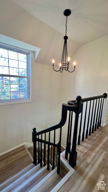 Staircase with wood finished floors, a chandelier, baseboards, and lofted ceiling