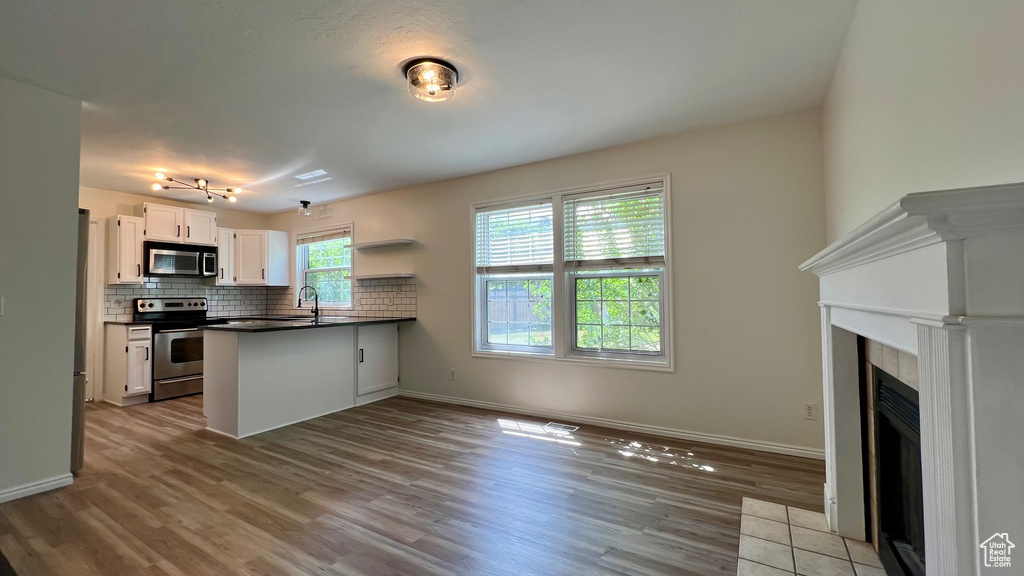 Kitchen with appliances with stainless steel finishes, a peninsula, dark countertops, wood finished floors, and white cabinetry