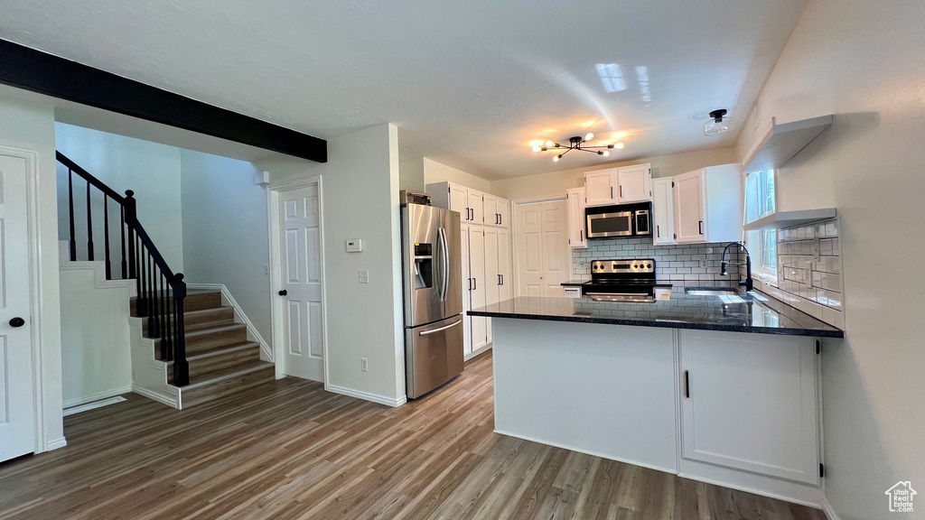 Kitchen featuring stainless steel appliances, a sink, a peninsula, backsplash, and wood finished floors