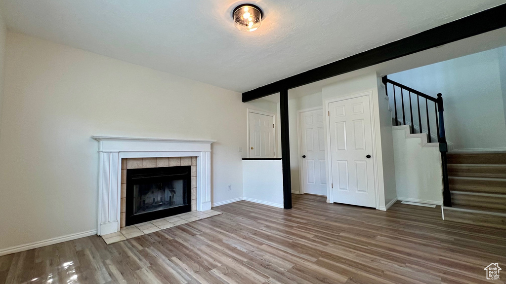 Unfurnished living room with wood finished floors, stairway, a tile fireplace, beamed ceiling, and baseboards