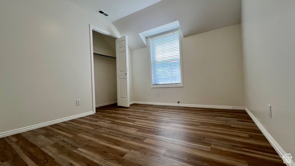 Unfurnished bedroom featuring wood finished floors, vaulted ceiling, baseboards, and a closet