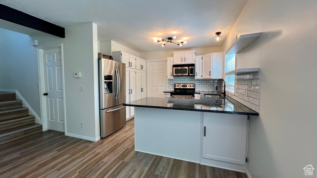Kitchen featuring stainless steel appliances, decorative backsplash, a peninsula, dark wood-style flooring, and baseboards