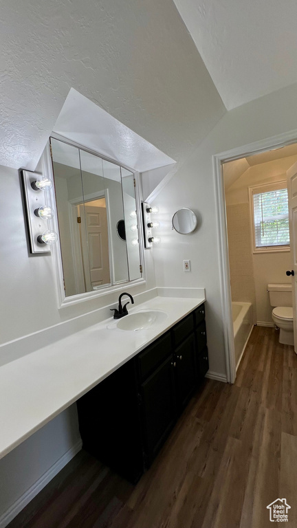 Full bath featuring wood finished floors, vanity, toilet, lofted ceiling, and a textured ceiling