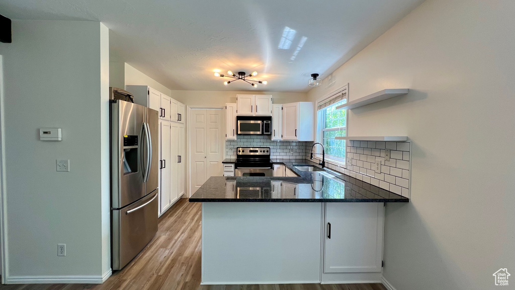 Kitchen with stainless steel appliances, a sink, open shelves, a peninsula, and tasteful backsplash
